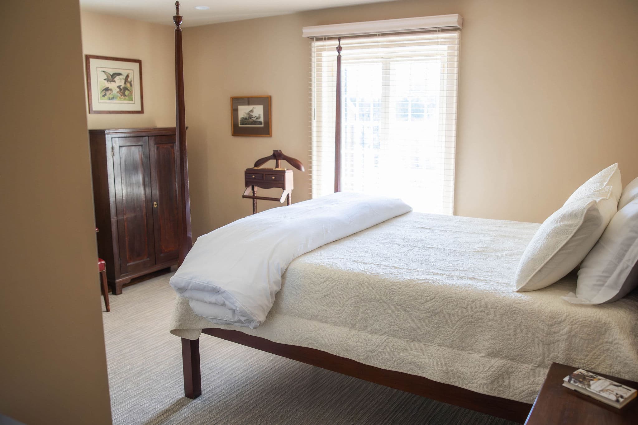 A cozy bedroom featuring a four-poster bed, a wooden wardrobe, and natural light from a window.