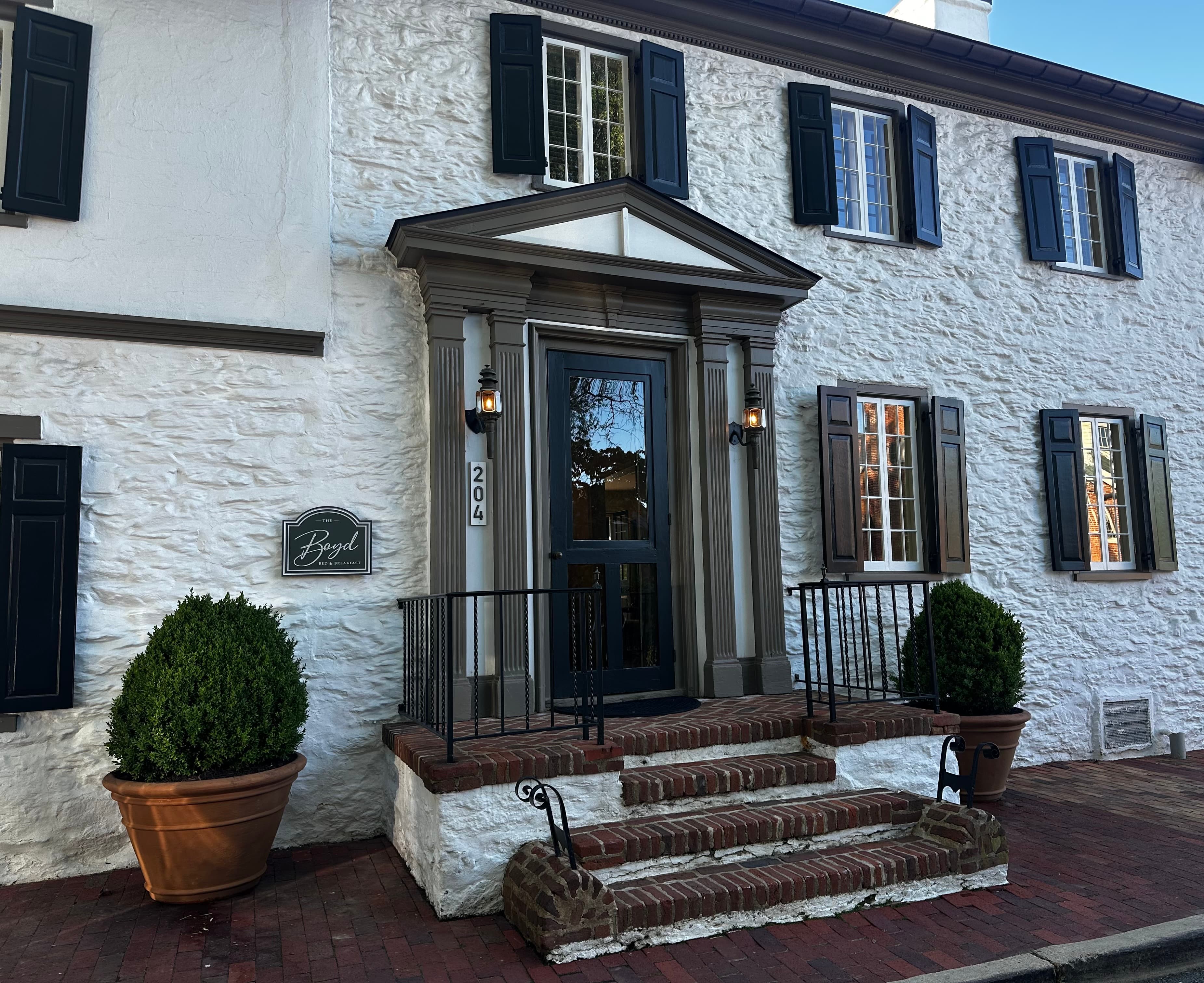 Exterior view of a white stone building with black shutters, featuring a prominent entrance and steps.