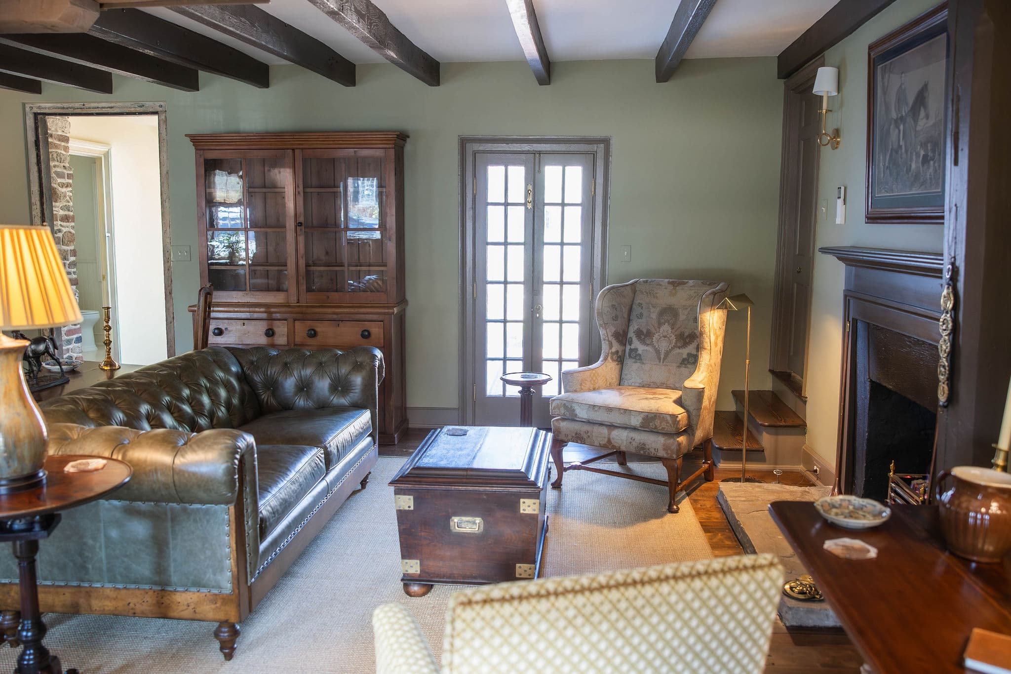 A cozy living room featuring a leather sofa, antique furniture, and a fireplace.